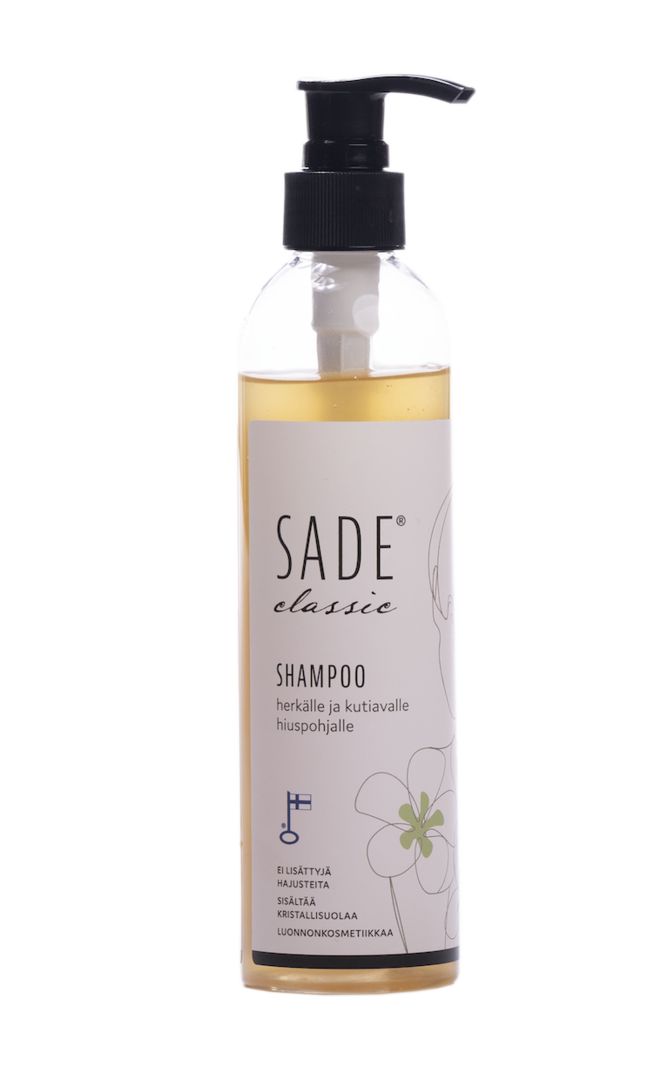 A clear bottle of SADE classic shampoo with a black pump, featuring Finnish text and a simple floral illustration on the label. The bottle is cylindrical, transparent, and has a glossy finish. The label uses clean sans-serif typography in black. Product stands alone against a plain light background, no people or actions shown.