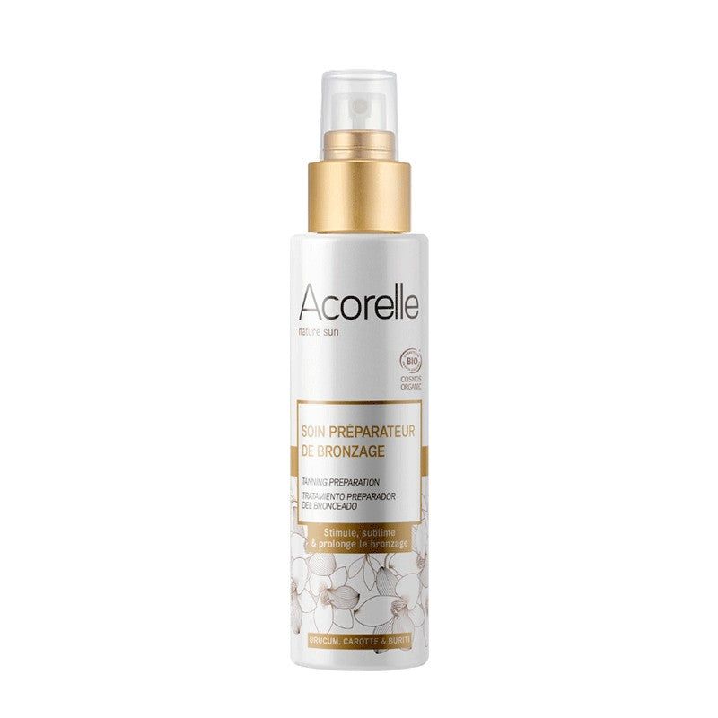 Acorelle Rusketukseen Valmistava Hoito: Nature Sun Soin Préparateur de Bronzage -suihkepullo kulta-valkoisella designilla ja kukkakoristein etiketissä; muovipullo on sylinterimäinen, läpinäkyvä korkki ja kiiltävä pinta; etiketissä groteskiteksti ja tuotetiedot mustalla; kuvattu valkoista taustaa vasten, ei ihmisiä tai käsiä näkyvissä.