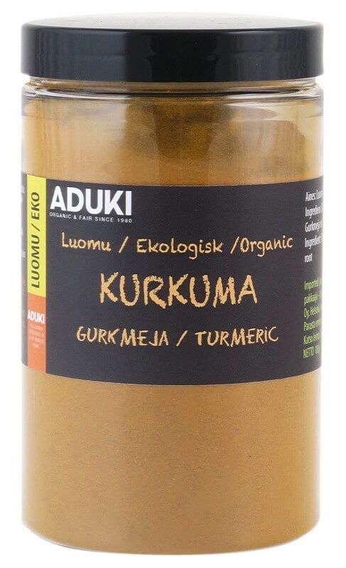 Aduki Luomu Kurkumajauhe; kirkas lieriömäinen lasipurkki mattamustalla muovisella kierrekannella; etiketissä lukee ADUKI Organic Turmeric useilla kielillä, painettu lihavoiduin kontrastisin groteskifontein valkoisella pohjalla; purkki sisältää hienoksi jauhettua kirkkaan keltaista kurkumajauhetta; useita luomusertifiointilogoja näkyvissä; tuote kuvattu valkoisella taustalla tasaisessa valaistuksessa, ei ihmisiä tai käsiä.