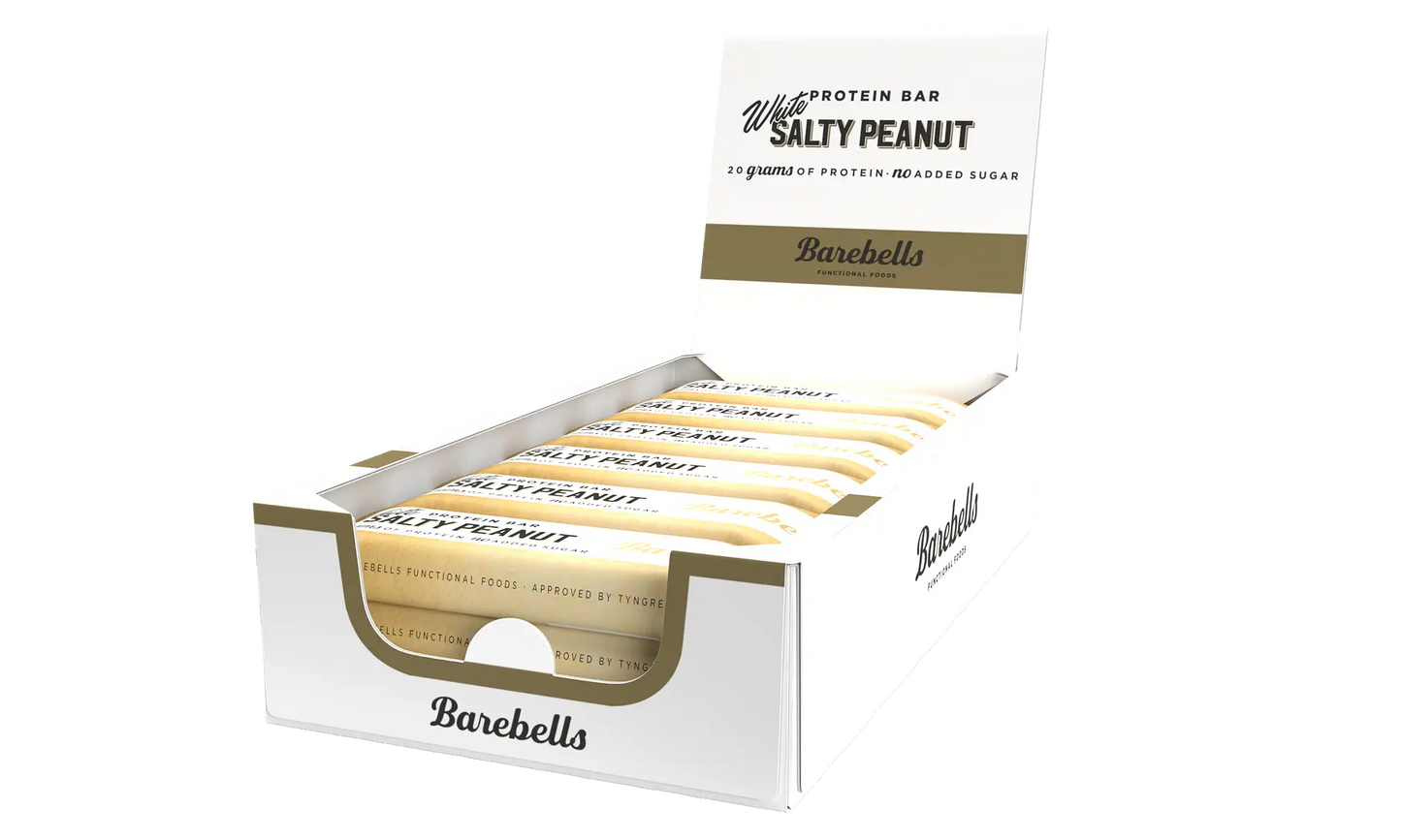 Barebells White Salty Peanut Proteiinipatukka; rasia Barebells Salty Peanut -proteiinipatukoita avoimena, sisällä useita yksittäin käärittyjä suorakulmaisia patukoita; ulompi rasia mattavalkoisella pinnalla kultaista ja mustaa lihavoitua groteskitekstiä, kertoo Salty Peanut -maun; ei ihmisiä tai käsiä; tuote kuvattu tasaista taustaa vasten yksinkertaisesta kuvakulmasta.