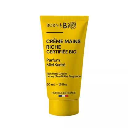 Keltainen Born to Bio -käsivoideputkilo, jossa lukee Crème Mains Riche Certifiée Bio hunaja-sheavoituoksulla, koko 50 ml, tekstiä ranskaksi ja englanniksi; putkilossa valkoinen läppäkorkki ja mattapinta; päätuotenimi lihavoidulla groteskikirjasimella, lisätiedot pienemmällä fontilla; ei ihmisiä tai käsiä näkyvissä; tausta yksinkertainen ja neutraali; suoraan edestä otettu tuotekuva.
