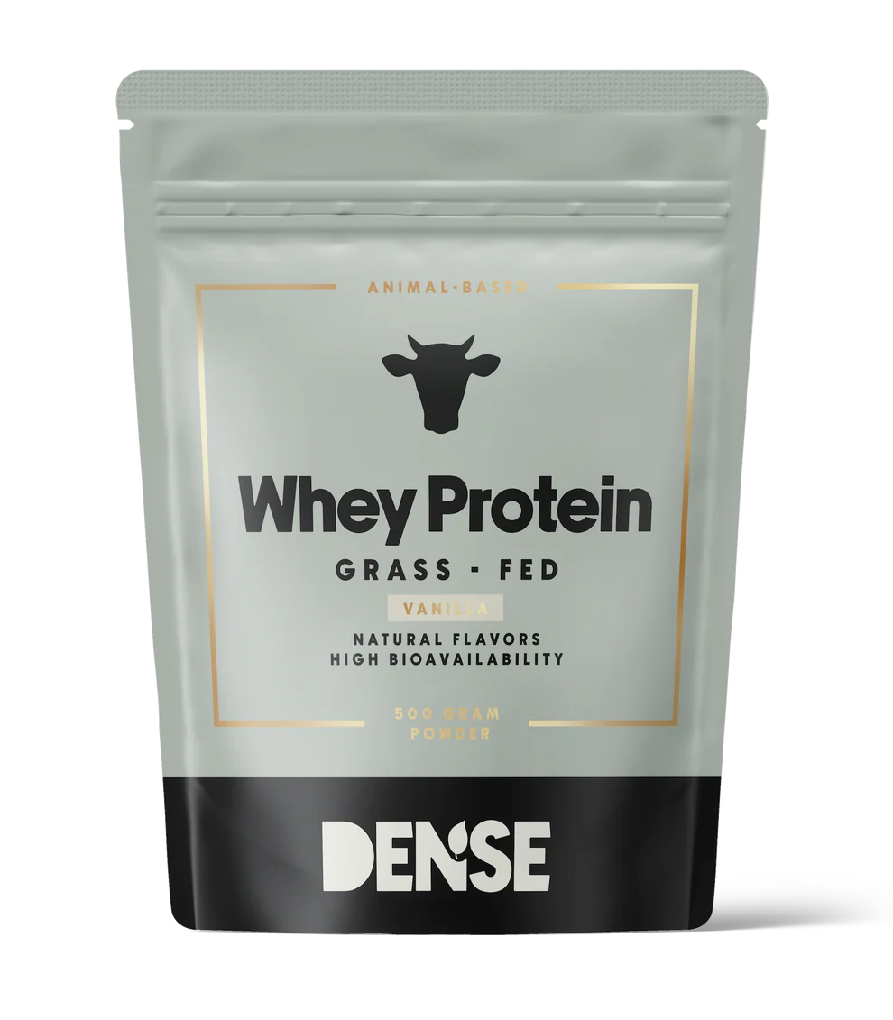DENSE Heraproteiini Vanilja; harmaa ja musta mattapintainen pussi suorakulmaisella muodolla, merkissä Dense yläreunassa, teksti kertoo Whey Protein, Grass-Fed, Vanilla; yksinkertainen lehmäkuvake tekstin alla; pussi korostaa luonnollisia makuja ja korkeaa biosaatavuutta laiduntavista lähteistä groteskifontilla; tuote seisoo pystyssä vaaleaa taustaa vasten, ei ihmisiä tai käsiä näkyvissä.