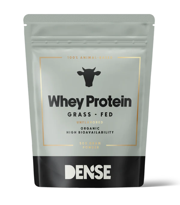 DENSE Luomu Heraproteiini Maustamaton; hopeanvärinen ja musta pussi, merkitty Whey Protein Grass Fed, lehmäkuvake, tekstissä kerrotaan maustamattomasta, luomulaadusta ja korkeasta biosaatavuudesta; DENSE-merkki lihavalla groteskifontilla; pakkauksessa ilmoitetaan 500 g proteiinijauhetta; mattapintainen, uudelleensuljettava, suorakulmainen pystypussi; tausta neutraali ja tasainen, ei ihmisiä tai esineitä näkyvissä.