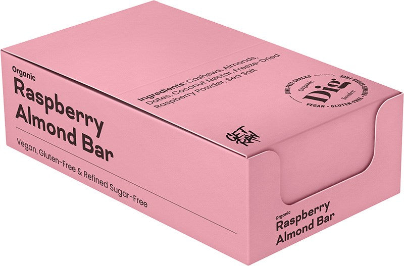 Dig Luomu Vadelma-Mantelipatukka; suorakulmainen vaaleanpunainen laatikko mattapinnalla, merkitty ”Organic Raspberry Almond Bar”; laatikossa teksti mainitsee vegaanisuuden, gluteenittomuuden ja puhdistetusta sokerista vapauden; pääasialliset ainesosat — mantelit, taatelit, kookospähkinä, merisuola ja pakastekuivattu vadelmajauhe — ovat lueteltuina; käytössä sekä antiikva- että groteskikirjasimia; ei ihmisiä tai rekvisiittaa näkyvissä; tausta yksivärinen.