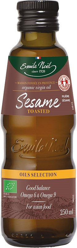 Emile Noel Luomu Paahdettu Seesamiöljy, ruskea lasipullo kiiltäväpintainen, sylinterimäinen ja kapea kaula; etiketissä vihreä-kultainen Emile Noel -brändäys, teksti "organic virgin oil", tilavuus 250 ml sekä maininta Omega 6 ja 9 rasvahapoista sekä sopivuudesta aasialaiseen ruokaan; ei ihmisiä eikä käsiä näkyvissä, tausta pelkistetty, kuva suoraan edestä silmän korkeudelta.