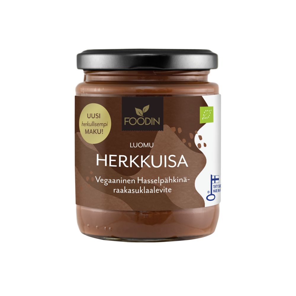 A jar of Foodin Herkkuisa vegan hazelnut-chocolate spread with Finnish text on the label, a gold lid, and a white background. The cylindrical glass jar has a smooth glossy surface. The label contains bold black and brown typography with additional small text lines. The shot is well-lit, showing only the product without any people or actions.