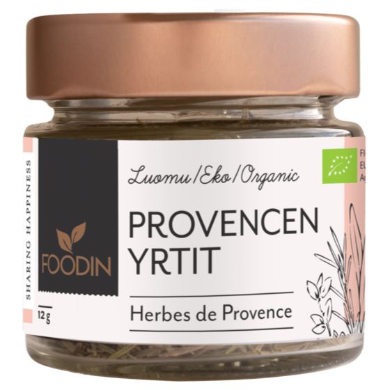 Foodin Luomu Provencen Yrtit (Herbes de Provence); lasipurkki ruusukultaisella metallisella kierrekannella, luomu/eko-merkintä ja viehättäviä yrttikuvituksia; lieriömäinen, läpinäkyvä purkki kuivattua yrttisekoitusta täynnä; paperietiketti mattapintainen, groteskifonttia, pientä lisätekstiä ja tyyliteltyjä kasvipiirroksia; vaalea tausta, ei ihmisiä.