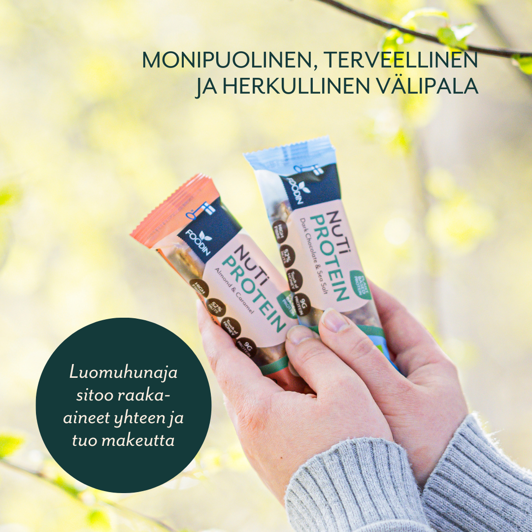Kaksi kättä pitelee kahta Foodin NUTI Luomu Pähkinäpatukka Protein -patukkaa ulkona, taustalla vihreitä lehtiä; mattapintaiset kääreet, joissa lihavoitu groteskikirjasin; pakkauksessa suomenkielistä tekstiä ja maininta proteiinipitoisista raaka-aineista sekä luomuhunajasta makeutusaineena; lähikuva tuotteesta ja käsistä.