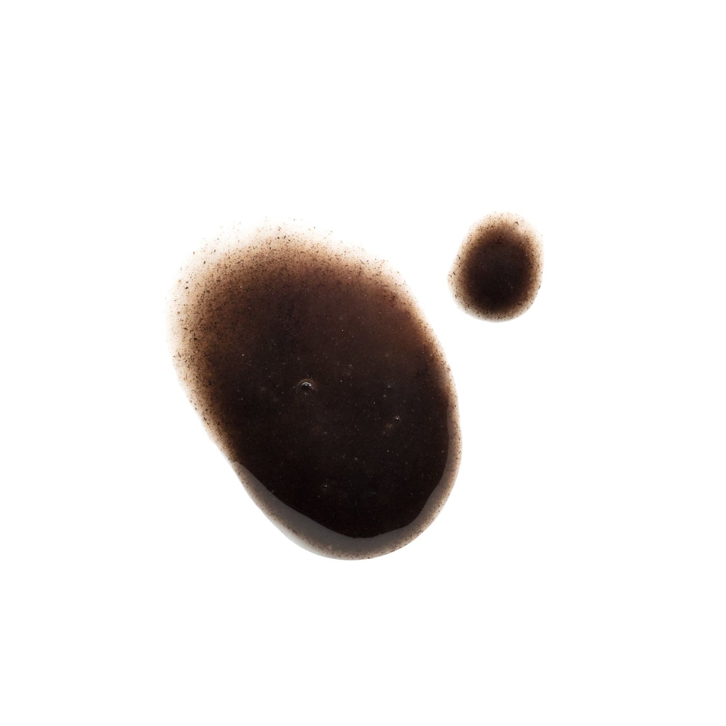 Two irregular, dark brown, glossy balsamic drops with specks, on a white background. No visible packaging or labels. Matte white backdrop with no additional elements. Close-up shot. No people or actions shown.