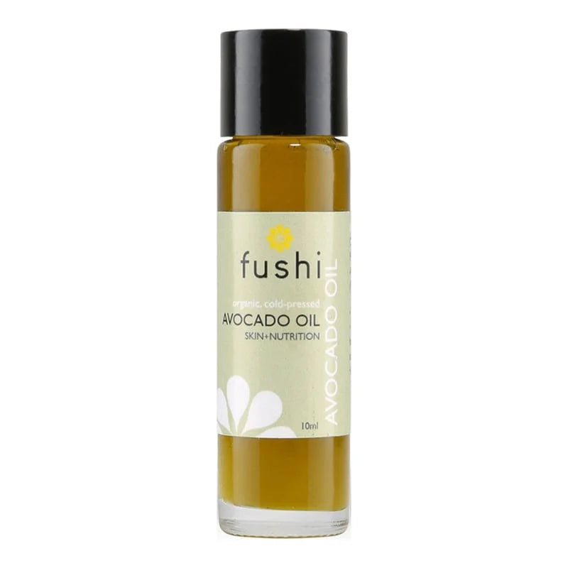 Fushi Luomu Avokadoöljy; pieni lasipullo, jossa musta korkki ja kellanvihreää öljyä; etiketissä valkoinen kukkakuvio ja teksti Fushi Avocado Oil Skin+Nutrition sekä maininta luomu, kylmäpuristettu avokadoöljy; lieriömäinen muoto, kiiltävä pinta, selkeä groteski kirjasin; valkoinen tausta, ei käsiä tai ihmisiä, suoraan edestä kuvattu tuotekuva.