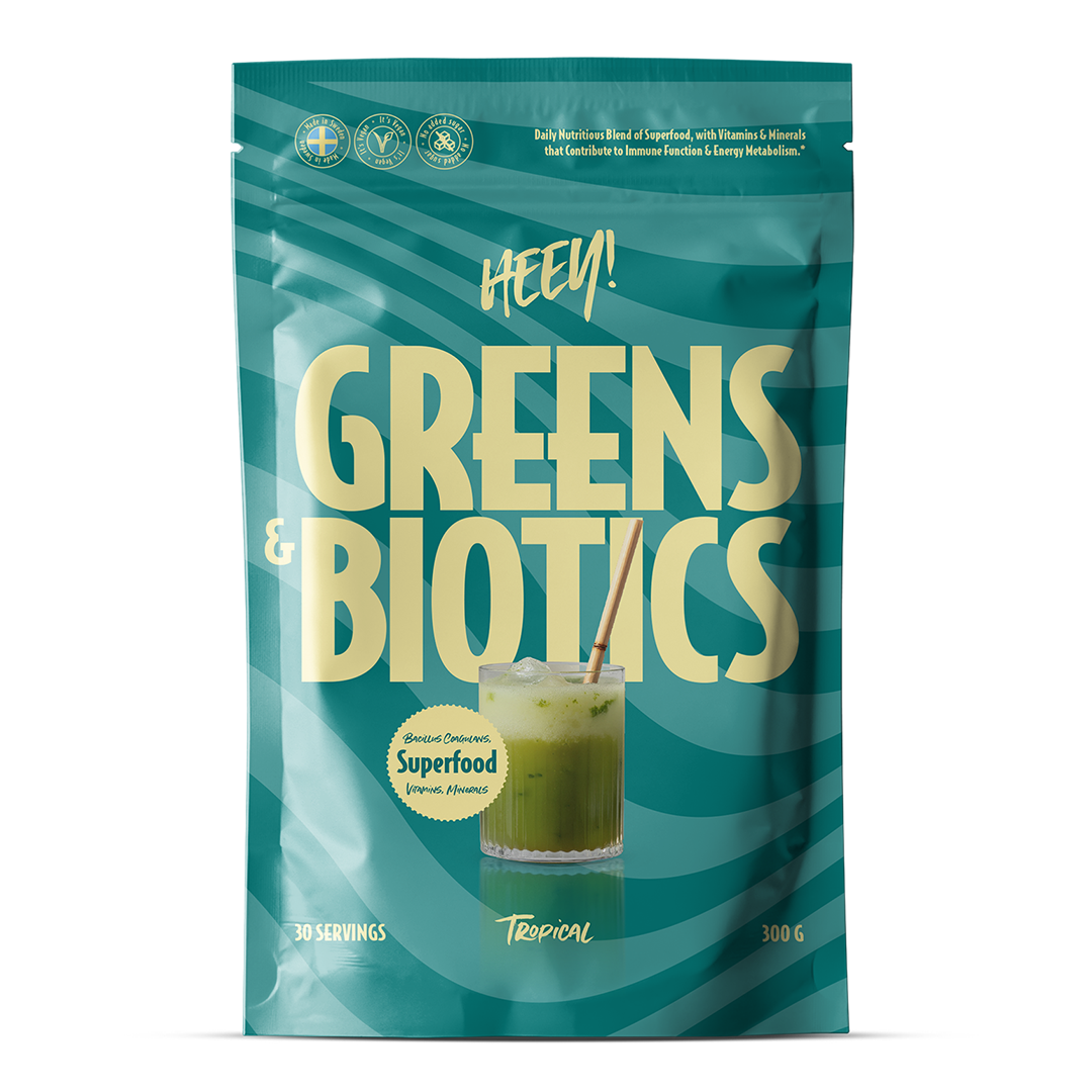 Heey! Greens & Biotics Superfood Tropical; sinivihreä pussi, jossa lukee Hey! Greens & Biotics, sisältää trooppista superfood-jauhetta probiooteilla; pakkauksessa kuva lasista vihreää juomaa pillin kera ja terveyshyötyjä kuvaavia kuvakkeita; nettopaino 300 g, 30 annosta; suorakulmainen, uudelleensuljettava mattapussi valkoisella modernilla groteskitekstillä; selkeä tuotenimi ja annostiedot; kuvituselementtejä etupuolella; tausta neutraali, ei ihmisiä kuvassa.