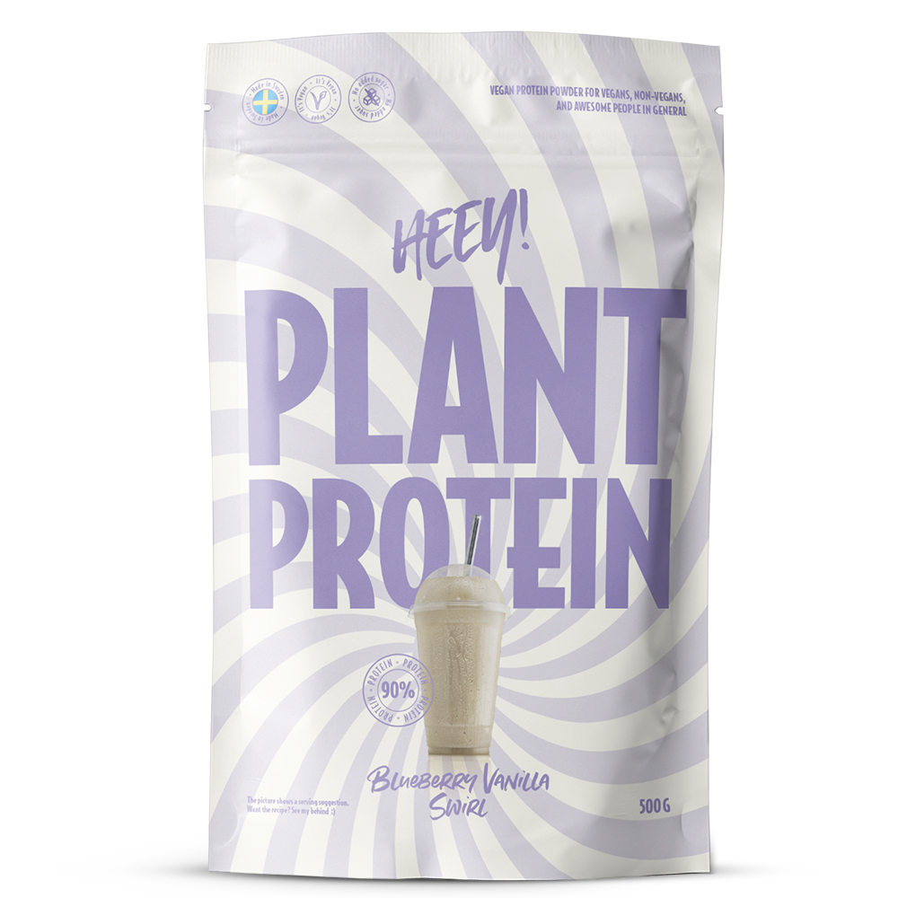 Heey! Plant Protein Blueberry Vanilla Swirl; valkoinen ja laventelinvärinen pyörremallinen pussi, jossa lukee Heey! Plant Protein, maku mustikka-vanilja ja kuva proteiinijuomasta; 500 g:n pakkaus korostaa kasvipohjaisia ainesosia; mattapintainen muovipakkaus, pystysuora suorakulmainen pussi suljetulla yläreunalla, luettavaa groteskitekstiä eri fonttikoin; etuetiketissä näkyy merkin nimi ja tuotetiedot; ei ihmisiä tai käsiä näkyvissä; pussi kuvattu vaaleaa taustaa vasten studiotuotekuvassa.