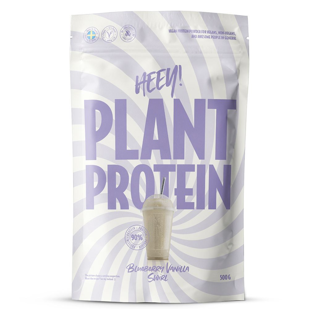 Heey! Plant Protein Blueberry Vanilla Swirl; valkoinen ja laventelinvärinen pyörremallinen pussi, jossa lukee Heey! Plant Protein, maku mustikka-vanilja ja kuva proteiinijuomasta; 500 g:n pakkaus korostaa kasvipohjaisia ainesosia; mattapintainen muovipakkaus, pystysuora suorakulmainen pussi suljetulla yläreunalla, luettavaa groteskitekstiä eri fonttikoin; etuetiketissä näkyy merkin nimi ja tuotetiedot; ei ihmisiä tai käsiä näkyvissä; pussi kuvattu vaaleaa taustaa vasten studiotuotekuvassa.