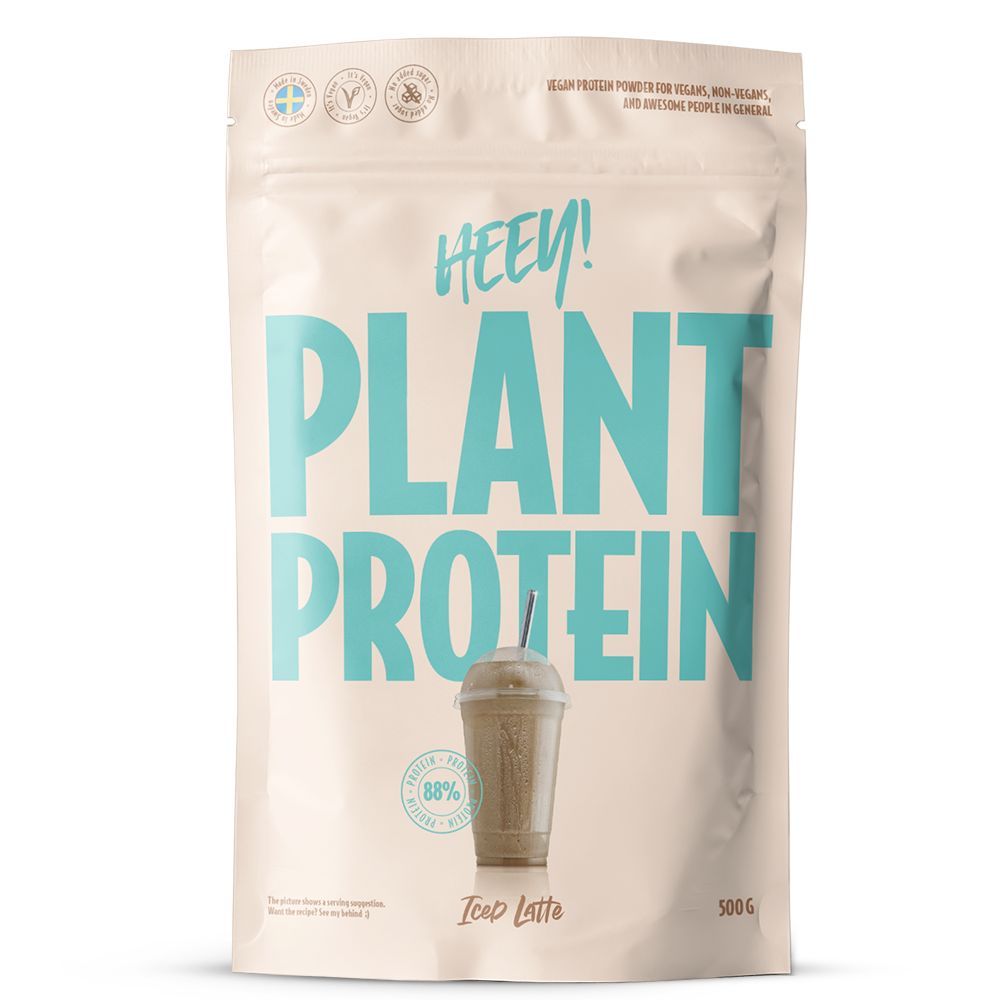 Heey! Plant Protein Iced Latte; beige 500 g:n pussi, jossa lukee HEEY! PLANT PROTEIN suurin sinivihrein kirjaimin, kuvituksena kylmä latte kupissa pillin kera etupuolella; pussin pinta on mattapintainen, muoto suorakulmainen pyöristetyin reunoin; pakkauksen teksti mainitsee vegaaniset ainesosat ja korkean proteiinipitoisuuden; ei ihmisiä tai käsiä näkyvissä, kuva on pelkkä tuotekuva neutraalia taustaa vasten.