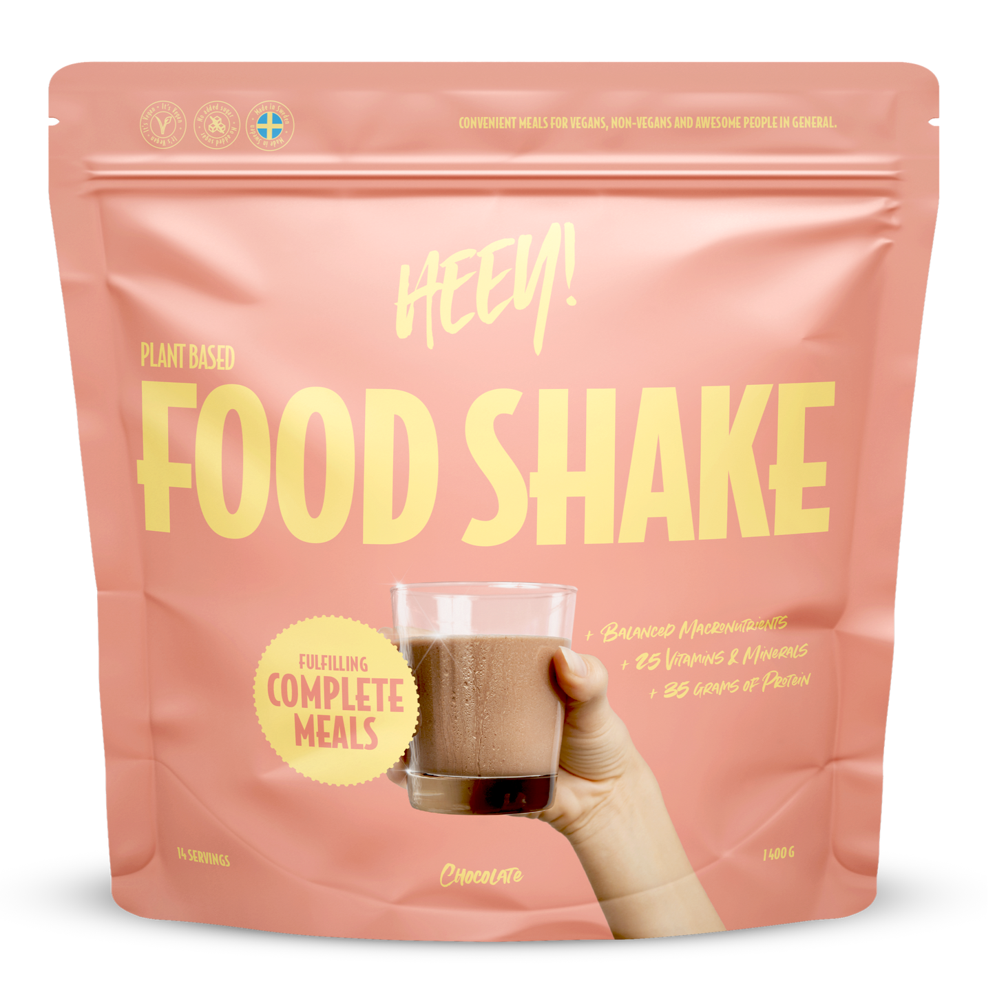 Heey! Vegan Food Shake, maku Chocolate; vaaleanpunainen mattapussi tekstillä Heey! Food Shake, pystyssä, etuosassa painettu kuva lasista tummanruskeaa suklaisen shaken näköistä nestettä; suurta ja pienempää valkoista groteskitekstiä etuosassa; avainlauseita plant-based, complete meals, 25 vitamins ja 35g protein; vaalea tausta, ei ihmisiä tai lisärekvisiittaa kuvassa.
