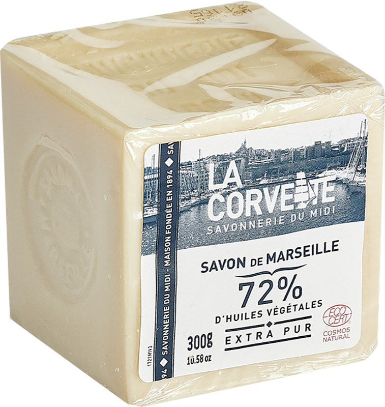 La Corvette Marseille Palasaippua Extra Pur; kuutionmuotoinen La Corvette Savon de Marseille -saippuapala kirkkaassa pakkauksessa, merkitty ”72% d'huiles végétales”, paino 300 g; oliivinvihreä saippua mattapinnalla ja neliskulmainen muoto, toisella sivulla leimattu kuvio; etiketissä kuvitus Marseillesta; ei ihmisiä tai muita taustaelementtejä näkyvissä.