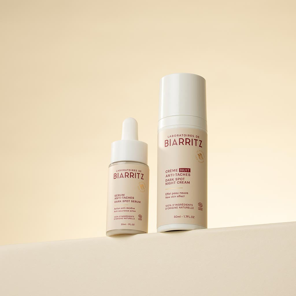 Laboratoires de Biarritz Anti Dark Spot Serum: kaksi ihonhoitotuotetta rinnakkain vaaleanbeigellä pinnalla – pigmenttimuutoksia hoitava seerumi läpikuultavassa, huurteisessa sylinterimäisessä pullossa valkoisella tiputinkorkilla, sekä kirkastava yövoide läpinäkymättömässä valkoisessa pumppupullossa; molemmissa yksinkertainen etiketti mustalla groteskitekstillä; ei ihmisiä tai muita esineitä kuvassa.