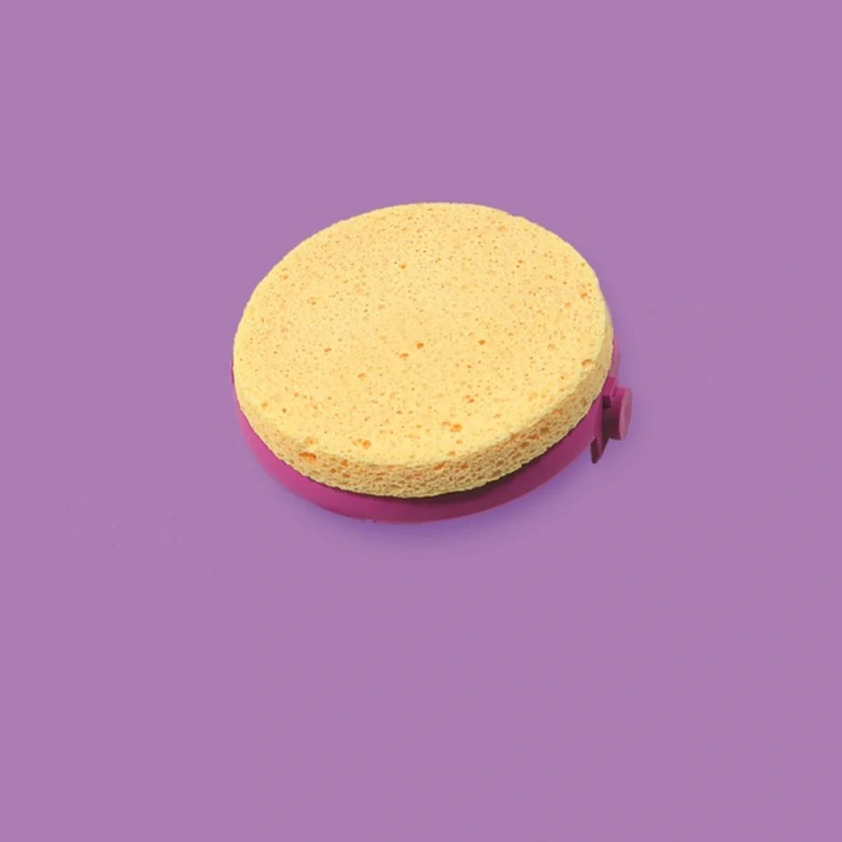 Roll Easy Voiteidenlevittäjä; pyöreä, keltainen sieni lepää tasaisella violetilla pinnalla vaaleanpunaisen pyöreän jalustan varassa; ei näkyvää pakkausta tai etikettitekstiä; ei typografiaa näkyvissä; sienen pinta mattapintainen ja yhtenäisen värinen; violetti alusta yksivärinen ja myös mattapintainen; ei ihmisiä tai käsiä kuvassa; yksinkertainen pöytätasokuva silmien tasolta.