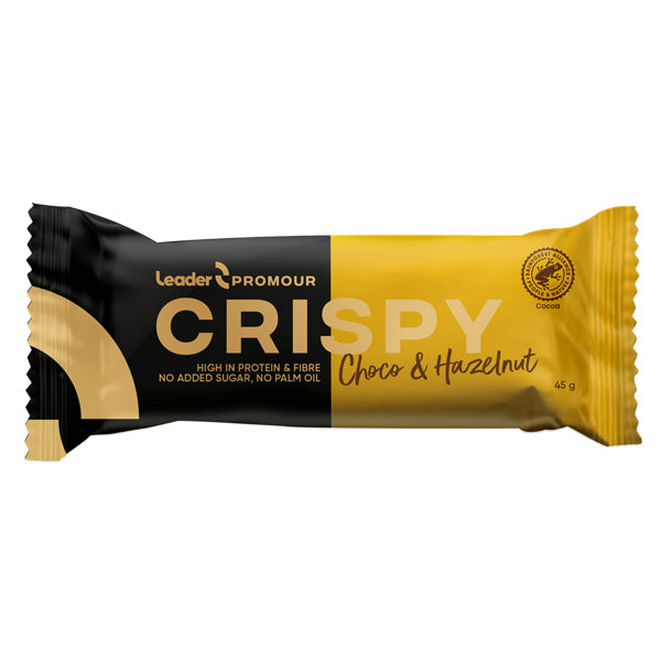Leader Promour Crispy Chocolate & Hazelnut -patukan keltainen ja musta kääre, 45 g; pakkaus korostaa runsasta proteiinia ja kuitua ilman lisättyä sokeria tai palmuöljyä; hasselpähkinä mainitaan keskeisenä raaka-aineena; kääre on kiiltäväpintainen lihavoidulla valkoisella ja mustalla groteskitekstillä; kuvakkeet korostavat tuoteominaisuuksia; ei ihmisiä tai käsiä näkyvissä, tausta yksinkertainen, tuote kuvan keskellä.