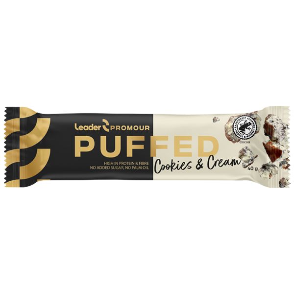 Leader Promour Puffed Cookies & Cream -proteiinipatukka mustassa ja beigessä mattapakkauksessa, suorakulmainen suljetuin reunoin. Pakkauksessa on suuret versaalikirjaimet tuotenimelle, pienempi teksti kuidusta, proteiinista, ilman lisättyä sokeria tai palmuöljyä. Patukka ja useita keksi-kerma-palasia on aseteltu vaalealle tasaiselle alustalle. Ihmisiä tai käsiä ei näy.