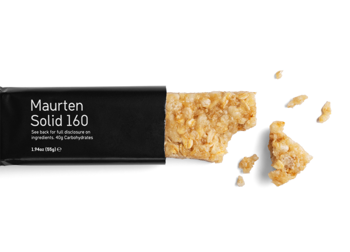 Maurten Solid 160 (40-pack): Maurten Solid 160 -energiapatukka on osittain avattu ja siitä puuttuu pala, useita pieniä murentuneita palasia on hajallaan lähellä; pakkaus on mattamusta valkoisella, lihavoidulla groteskitekstillä, joka näyttää brändin ja tuotenimen; patukka on suorakulmainen ja hieman karheapintainen; kaikki on aseteltu valkoiselle taustalle suoraviivaisessa tuotekuvassa.