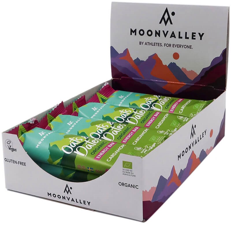 Moonvalley Luomu Energiapatukka Kardemumma; rasia Moonvalley Oats & Dates -energiapatukoita, merkitty luomuksi, gluteenittomaksi ja vegaaniseksi, värikkäällä vuoriaiheisella pakkauksella; suorakulmainen rasia mattapinnalla ja monivärisin vuorikuvituksin; useita vihreäkääreisiä patukoita näkyvissä avoimessa rasiassa; etikettiteksti groteskilla; valkoinen tausta, ei ihmisiä tai esineitä.