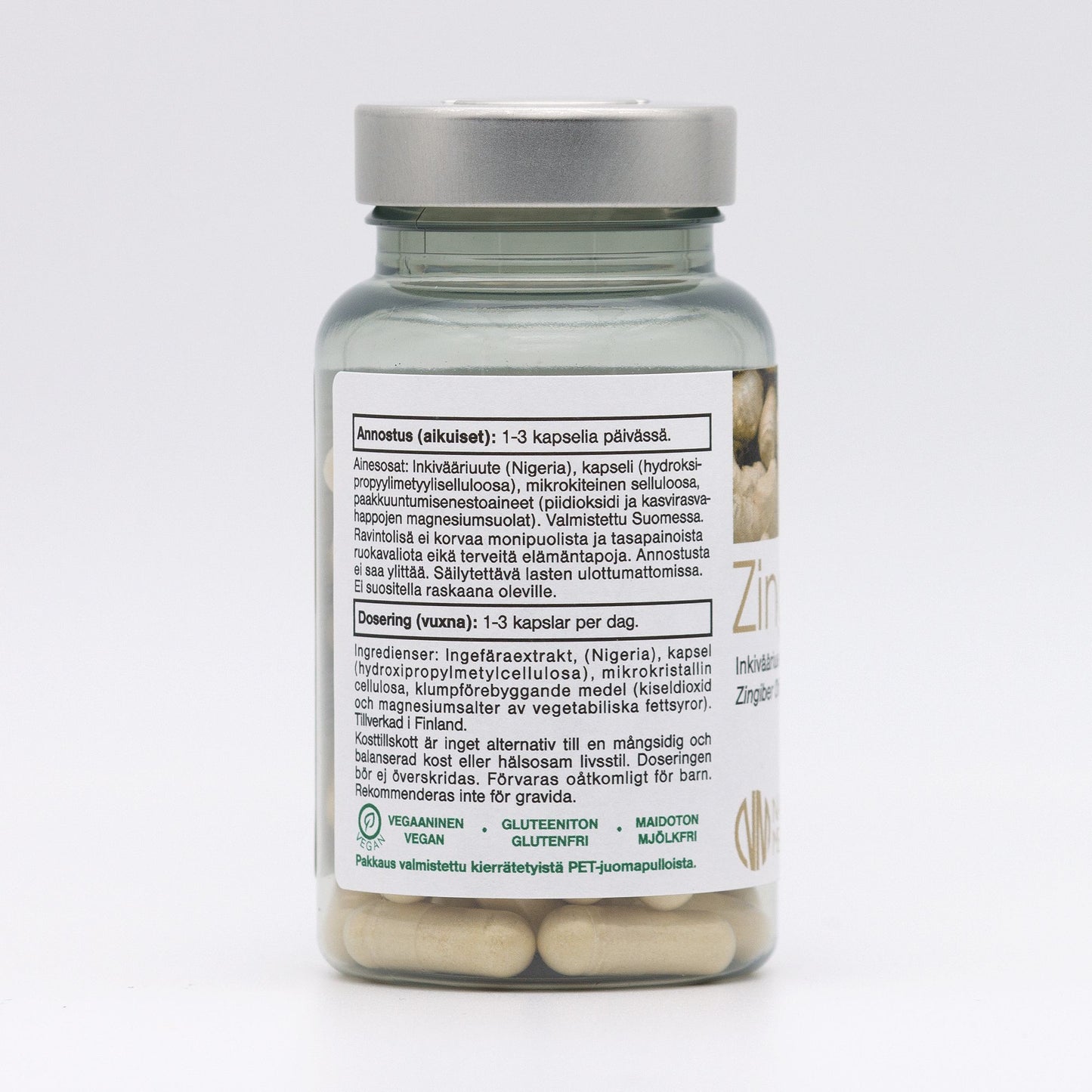 A bottle of zinc supplement capsules is shown. The plastic bottle has a green, screw-on lid and a matte finish. The cylindrical label is white with black and green sans-serif text, clearly listing product details such as dosage and ingredients in Finnish, Swedish, and English. Visual symbols indicate vegan, gluten-free, lactose-free status. Photo background is plain white with soft even lighting. No people or hands are visible in the shot. A bottle of zinc supplement capsules with a label describing dosage