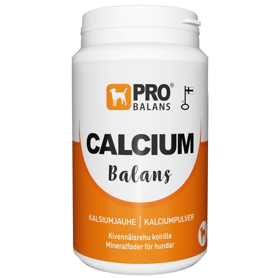 A white and orange container labeled PRO BALANS CALCIUM Balans with text in Finnish and Swedish, indicating it’s a calcium powder mineral supplement for dogs. The product is designed to help support your dog’s bone health. Plastic cylindrical jar with matte finish and screw-on lid, bold sans-serif typeface on label, no people or additional objects visible, plain neutral background, frontal product shot.