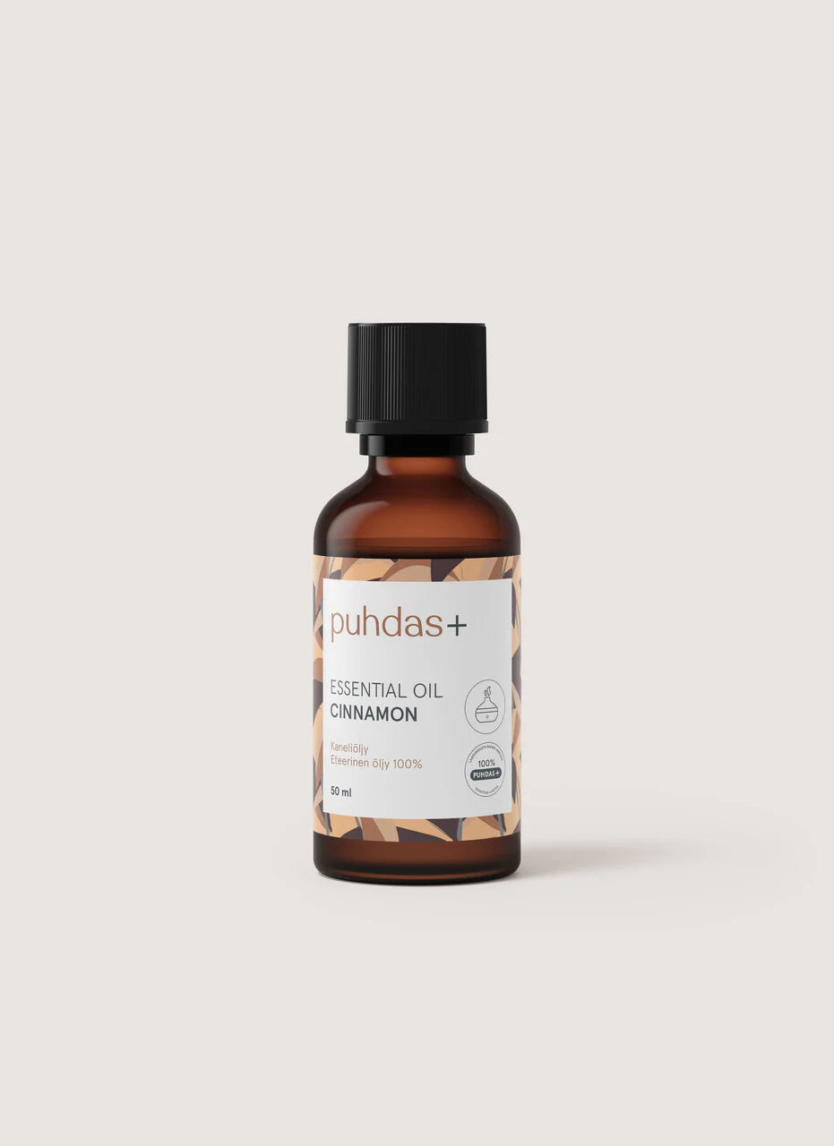 puhdas+ ESSENTIAL OIL CINNAMON -pullo, pieni meripihkanvärinen lasipullo mustalla muovikorkilla, pystyssä vaaleanbeigellä tasaisella taustalla; pullon pinta sileä ja kiiltävä; valkoisessa etiketissä mustaa ja ruskeaa tekstausvapaata tekstiä sekä geometrisia ruskeita kuvioelementtejä alaosassa; ei ihmisiä tai toimintaa kuvassa.