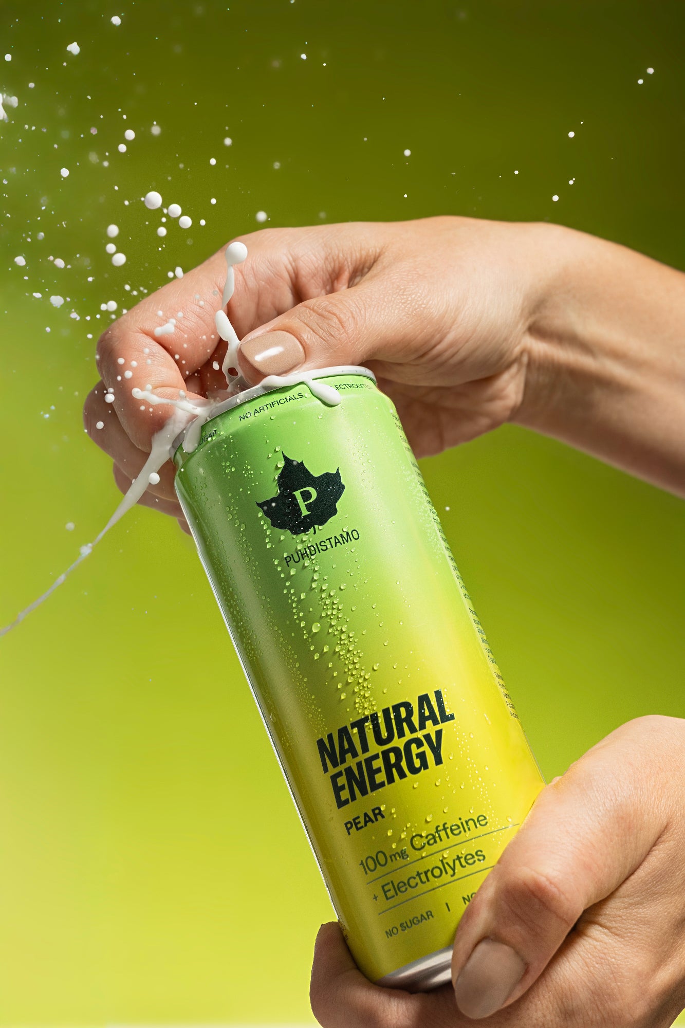 Puhdistamo Natural Energy Pear; käsi avaa päärynmakuisen energiajuomatolkun, nestettä suihkuaa voimakkaasti ylöspäin tasaista neutraalia taustaa vasten; tolkussa matta pinta vihreässä ja keltaisessa värissä; etikettitekstissä mainitaan kofeiini, elektrolyytit ja sokerittomuus selkeällä palkkikirjasimella; tausta liukuvärein vihreästä keltaiseen tolkun värejä mukaillen; lähikuva, käsi avausrenkaan kohdalla.