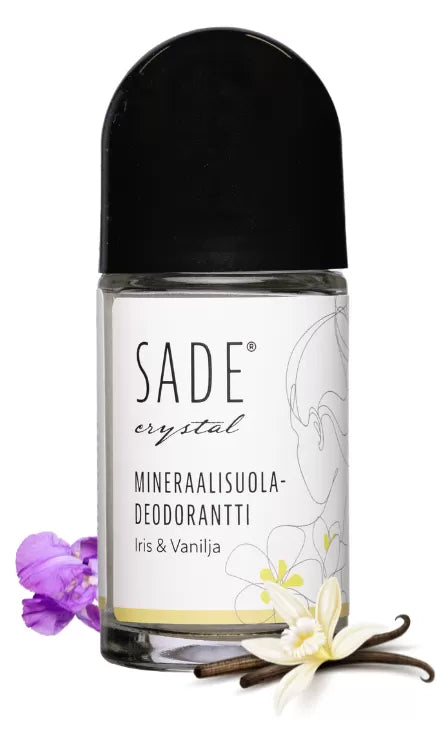 Sade Mineraalisuoladeodorantti Roll-On Iris & Vanilja; kirkas roll-on-deodoranttipullo valkoisella korkilla, etiketissä teksti "SADE crystal Mineraalisuola-Deodorantti Iris & Vanilja" yksinkertaisella sans-serif-typografialla; pakkauksessa painettuja kukkakuvituksia ja vaniljapalko sekä oikeita violetteja ja valkoisia kukkia vieressä; tausta valkoinen; ei ihmisiä tai käsiä; pinta kiiltäväpintainen.