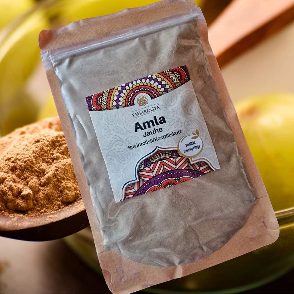 Saharogya Amla jauhe; sinetöity pakkaus värikkäällä etiketillä hienojakoista jauhetta sisältävän kulhon vieressä, taustalla tuoreita vihreitä amla-hedelmiä; mattapintainen ja suorakulmainen pakkaus, suuri lihavoitu groteskiteksti keskellä monivärisin grafiikoin ympäröitynä; neutraali tausta, ei ihmisiä tai käsiä.