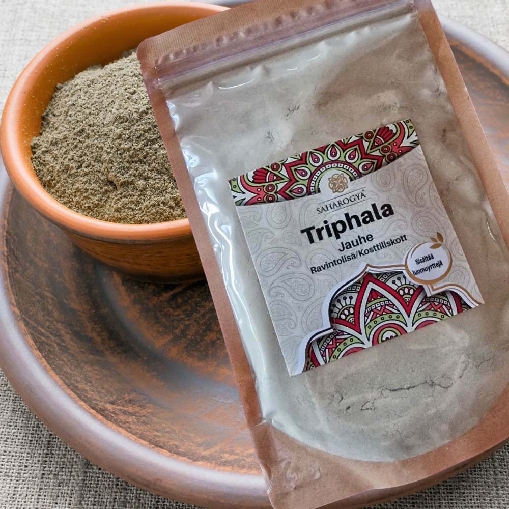 Saharogya Triphala jauhe; ruskea kulhollinen Triphala-jauhetta pyöreällä luonnonpuisella lautasella, vieressä mattapintainen uudelleensuljettava pystypussi värikkäin grafiikoin ja tekstillä "Triphala Jauhe" lihavoiduin selkein kirjaimin; kaikki aseteltu beigelle tekstiilipinnalle; ei ihmisiä tai toimintaa; ayurvedinen seos edustaa perinteistä luonnollista hyvinvointia.