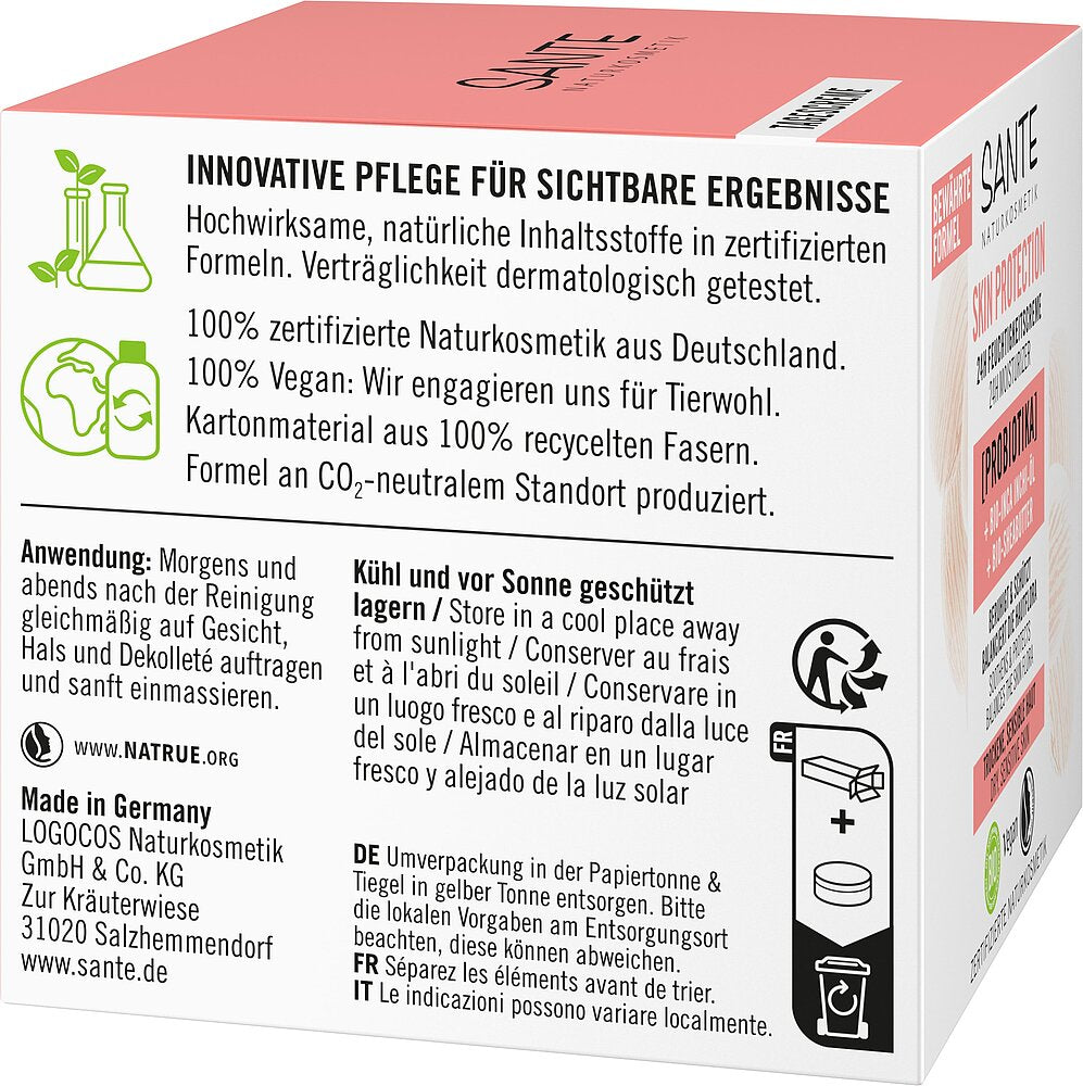 Sante Skin Protection 24h Kosteusvoide; valko-vaaleanpunainen Sante-kosmetiikkalaatikko saksankielisin tekstein, jotka kuvaavat luonnollisia ainesosia, ympäristöystävällistä pakkausta, käyttöohjeita ja säilytysneuvoja sekä vegaanikuvakkeen; luomusertifiointilogot ja yritysbrändäys sivussa; laatikko on suorakulmainen mattapinnalla musta-vaaleanpunaisin groteskitypografioin; tausta on neutraali pinta; ei ihmisiä tai käsiä näkyvissä.