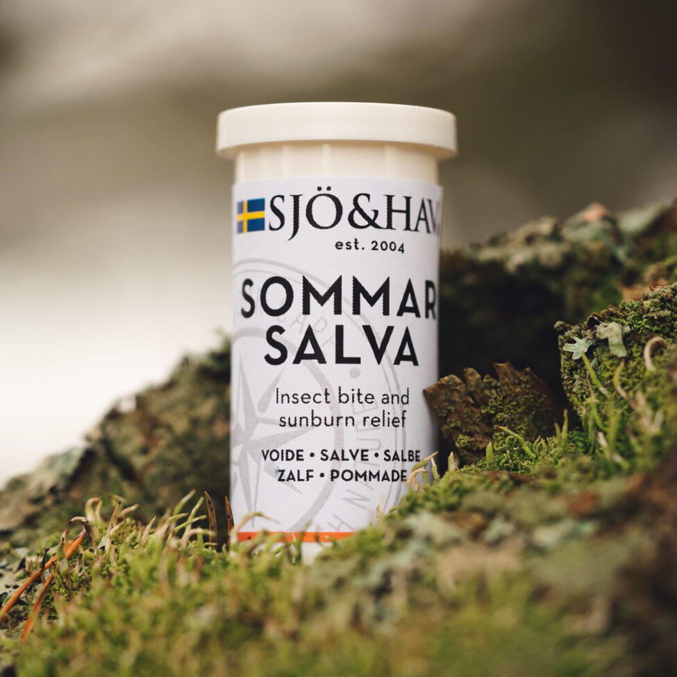 Pyöreä, metallinen Sjö&Hav Sommar Salva -purkki, jonka pinta on mattahopeanvärinen; purkki on aseteltu sammaleen ja harmaiden kivien joukkoon. Etiketissä on lihavoitua, pääteviivatonta mustaa ja oranssia tekstiä valkoisella pohjalla. Kuvassa näkyy vain purkin etuosa, ei ihmisiä eikä käsiä. Etiketti kertoo voiteen helpottavan hyönteisten pistoja ja auringon polttamaa ihoa.