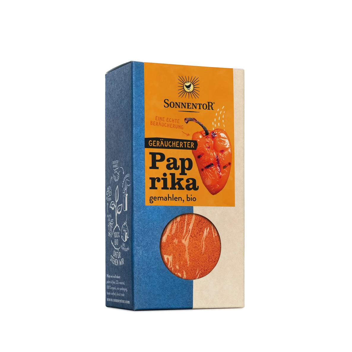 Suorakulmainen pahvilaatikko Sonnentorin luomusavupaprikaa seisoo pystyssä, mattapinnalla ja keskellä pyöreällä leikkausikkunalla, joka paljastaa oranssinpunaisen jauhemaisen mausteen sisällä. Etupaneelissa on yksityiskohtainen kuvitus yhdestä punaisesta paprikasta. Etikettiteksti on selkeällä painetulla fontilla yläosassa. Ihmisiä tai käsiä ei näy. Tausta on neutraali ilman selkeästi näkyviä lisäesineitä.