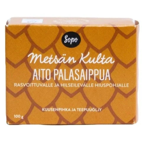 Sopo Metsän Kulta Aito Palasaippua; ruskea laatikko Sopo Metsän Kulta Aito Palasaippua -shampoosaippualle, kuvioinaan suomukuvio ja teksti, joka ilmoittaa tuotteen sopivan rasvaiselle ja hilseilevälle hiukselle sisältäen pihkaa ja teepuuöljyä, 100 g; laatikko suorakulmainen ja mattapintainen; etiketin typografia groteskinen eri painoin; tuote kuvattu lähikuvassa vaaleaa taustaa vasten, ei ihmisiä eikä käsiä näkyvissä.