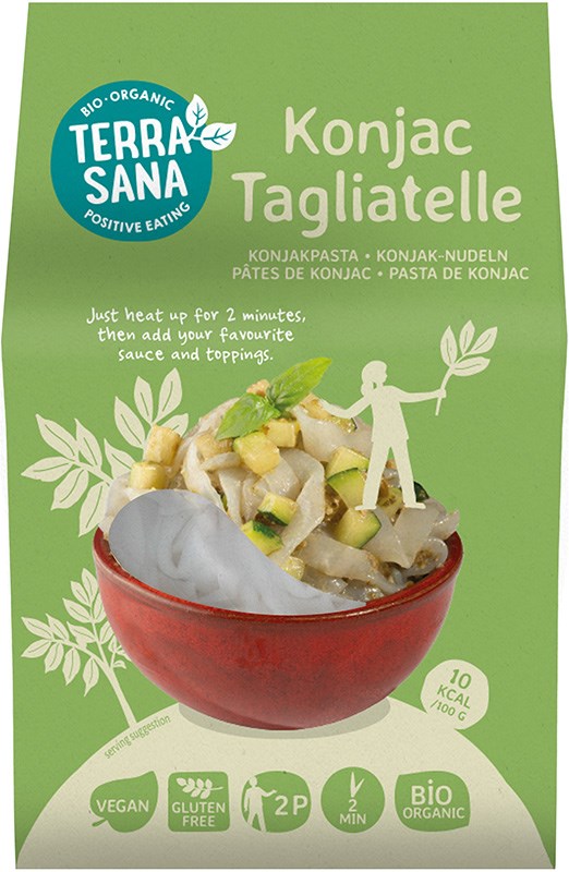 Terrasana Luomu Konjak Tagliatelle; vihreä muovipakkaus seisoo pystyssä mattapinnalla; etuosassa yksinkertaista groteskitekstiä ja kuvakkeita, jotka osoittavat vegaanisuuden, gluteenittomuuden, luomun, kahden annoksen koon ja 10 kcal per 100 g; pakkauksen vieressä keraaminen kulho, jossa nuudeleita ja viipaloituja vihanneksia näkyvissä; neutraali tausta, ei ihmisiä tai käsiä näkyvissä; laaja kuva keskittää molemmat kohteet kuvaan.