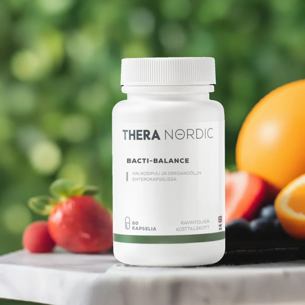 THERA Nordic Bacti-Balance; valkoinen lisäravinnepullo, jossa lukee "THERA NORDIC Bacti-Balance", seisoo pystyssä tasaisella pinnalla; pullo on sylinterinmuotoinen kierrekorkilla ja mattapinnalla; etiketissä sinistä ja harmaata groteskitekstiä; taustalla epätarkkana appelsiini, mansikka ja muita hedelmiä; kuvassa ei näy ihmisiä tai käsiä.