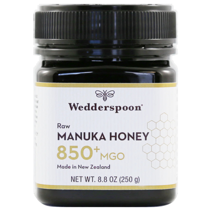 Wedderspoon Manuka-hunaja 850+ MGO; musta muovipurkki Wedderspoon Raw Manuka Honey 850+ MGO, 8,8 unssia (250 g), valkoinen etiketti hunajakennokuvioin ja selkeällä tekstillä, joka ilmoittaa Uuden-Seelannin alkuperän ja premium-laadun; etiketin fontit groteskia lihavoituna ja tavallisena painona; purkki mattapintainen, lieriömäinen muoto; tausta valkoinen ilman muita esineitä tai ihmisiä.