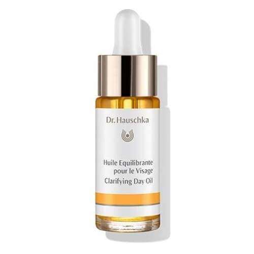 Dr. Hauschka Clarifying Day Oil -kasvoöljy tiputinkorkilla; ranskan- ja englanninkielistä tekstiä, keltertävää tasapainottavaa kasvoöljyä pullossa; kirkas, lieriömäinen lasipullo kiiltävällä pinnalla, valkoinen ja metallinkultainen tiputinkorkki; etiketissä groteskitekstiä, tuotenimi ja brändilogo; vaalea, neutraali tausta, ei ihmisiä tai käsiä; studiovalaistus pehmein heijastuksin lasin pinnalla.