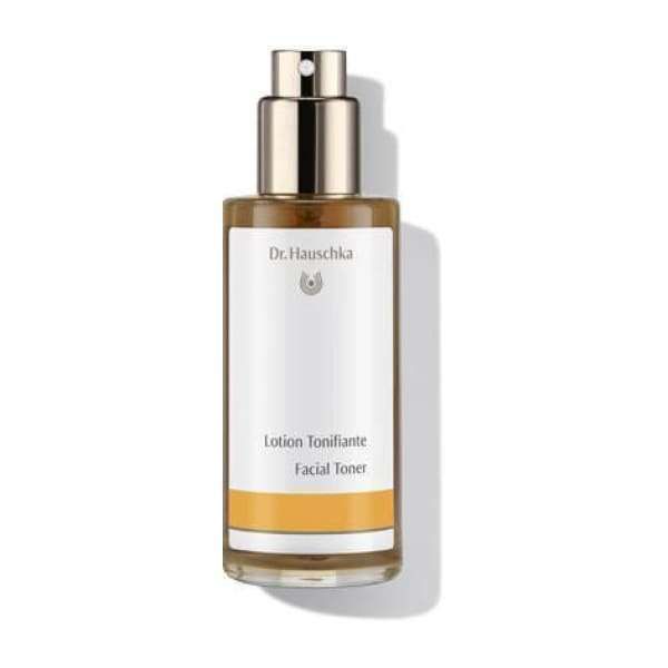 Dr. Hauschka Kasvovesi -pullo, lasinen, kulta-hopeinen suihkukorkki, valkoinen etiketti oranssein korostuksin; musta groteskiteksti "Dr. Hauschka Facial Toner", kiiltäväpintainen sylinterinmuotoinen pullo