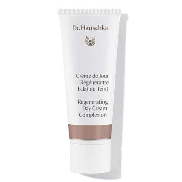 Dr. Hauschka Regenerating Day Cream Complexion -tuubi, valkoinen, teksti sekä ranskaksi että englanniksi ja ruskea nauha alaosan lähellä; tuubi sylinterimäinen mattapinnalla; korkki metallisen tai heijastavan hopeinen; typografia tekstausvapaata selkeällä hierarkialla tuotenimelle ja tiedoille; yksinkertainen tausta, ei muita esineitä, ihmisiä tai toimintaa näkyvissä; kuva näyttää koko tuotteen pystyssä ja keskitettynä.