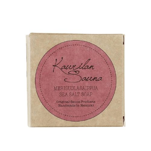 Kaurilan Sauna Merisuolasaippua; ruskea pakkaus pyöreällä vaaleanpunaisella etiketillä tekstillä "Kaurilan Sauna Merisuolasaippua Sea Salt Soap", alkuperäiset saunatuotteet käsintehty Helsingissä luonnollisista ainesosista; pakkaus suoralinjainen ja mattapintainen, suljettu; etiketin teksti valkoisella groteskikirjasimella; valkoinen tausta, ei ihmisiä tai käsiä kuvassa, silmän korkeudelta kuvattu.