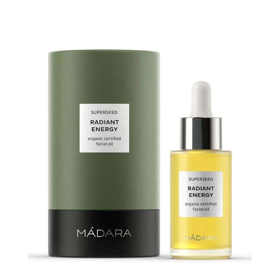 MÁDARA Superseed Kasvoöljy Radiant Energy -pullo ja pakkaus, kirkas lasipullo valkoisella tippakorkilla, korkea vihreä-musta sylinterinmuotoinen rasia; groteskiteksti "SUPERSEED Radiant Energy Organic Certified Facial Oil"