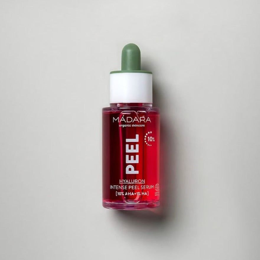 A red glass dropper bottle of MÁDARA PEEL Hyaluron Intense Peel Serum with a green cap, featuring hydrating hyaluronic acid, photographed against a plain light gray background. The bottle is cylindrical with smooth, glossy surfaces and a reflective finish. White sans-serif text appears on the label, which includes the product and brand name in all caps. No people or hands visible.
