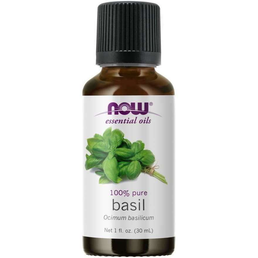 Now Foods Basilikaöljy; ruskea lasipullo valkoisella muovikorkilla, lieriömäinen muoto; mattaetiketissä luettavissa NOW-eteeriset öljyt, 100-prosenttinen basilika, tilavuus 1 fl. oz. (30 ml); etiketissä väriväris kuva tuoreista vihreistä basilikanlehdistä sekä violettia, mustaa ja vihreää groteskitekstiä eri kokoina; vaalea studiotausta.