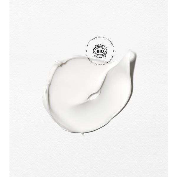 Patyka Pro-Collagen Lift Mask Kasvonaamio; kierre paksua valkoista voidetta levitettynä matalle valkoiselle tekstuuripinnalle; yläpuolella pyöreä vihreä luomusertifiointileima, jossa sana "organic" selkeästi näkyvissä; ei pakkausta, ihmisiä tai käsiä kuvassa; lähikuva korostaa tuotteen sertifioitua luomualkuperää.