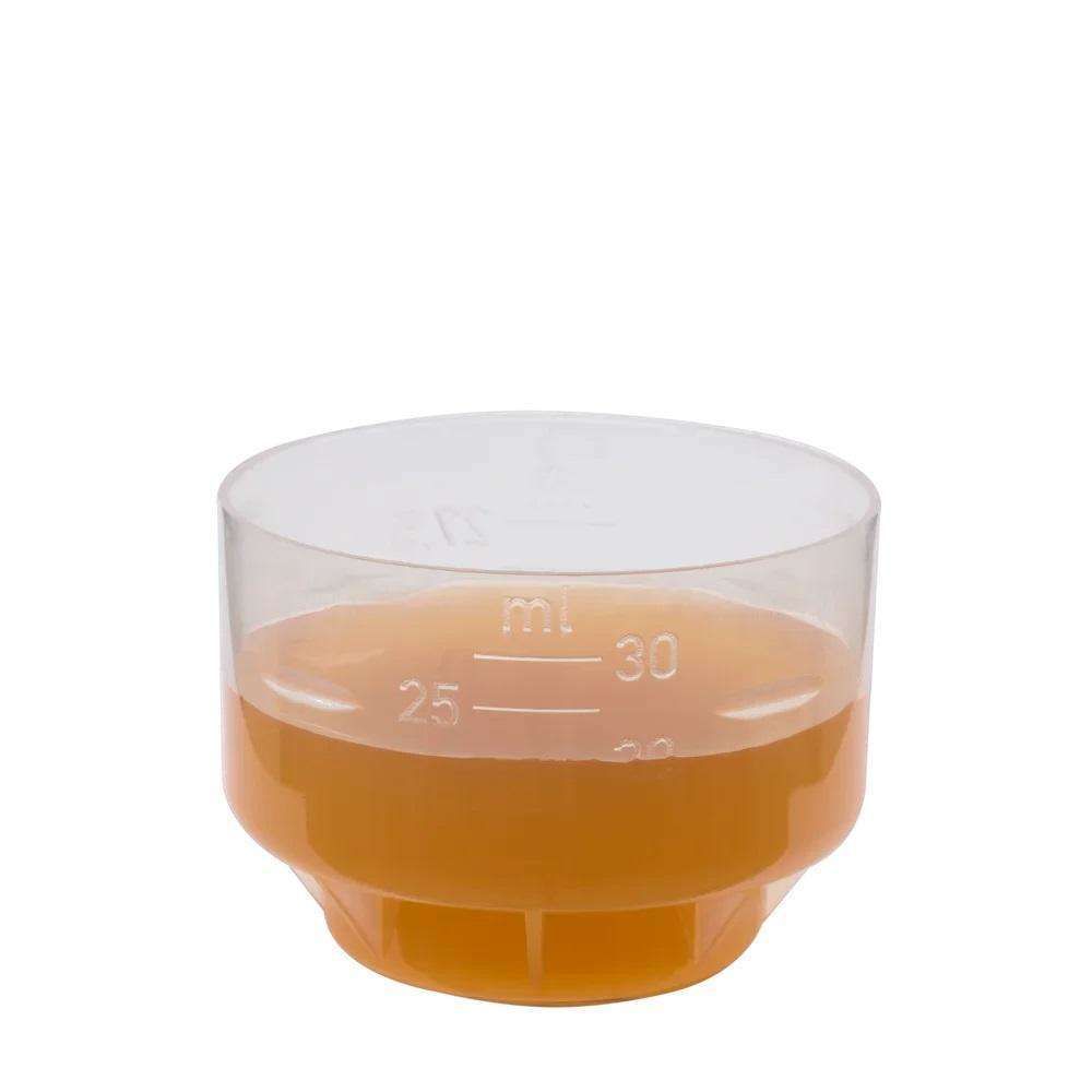 Kirkas mittalasi täytettynä appelsiinimehulla 25 ml:n merkkiin asti valkoisella taustalla; läpinäkyvä sylinterinmuotoinen kiiltäväpintainen mitta-astia, pystysuuntaiset mitta-asteikot pienellä groteskitekstillä