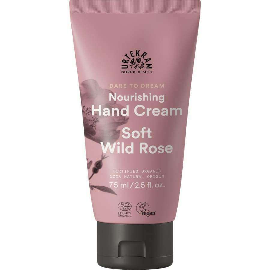 Urtekram Dare to Dream Soft Wild Rose Käsivoide; vaaleanpunainen tuubi tekstillä "Urtekram Nourishing Hand Cream, Soft Wild Rose, 75 ml", merkitty sertifioiduksi luomuksi ja vegaaniseksi; tuubi mattapintainen, hienovarainen ruusukuvitus etiketin lähellä; musta kierrekorkki; luettavissa brändi- ja tuotenimi yksinkertaisella groteskityypillä; ei ihmisiä tai taustaympäristöä kuvassa.
